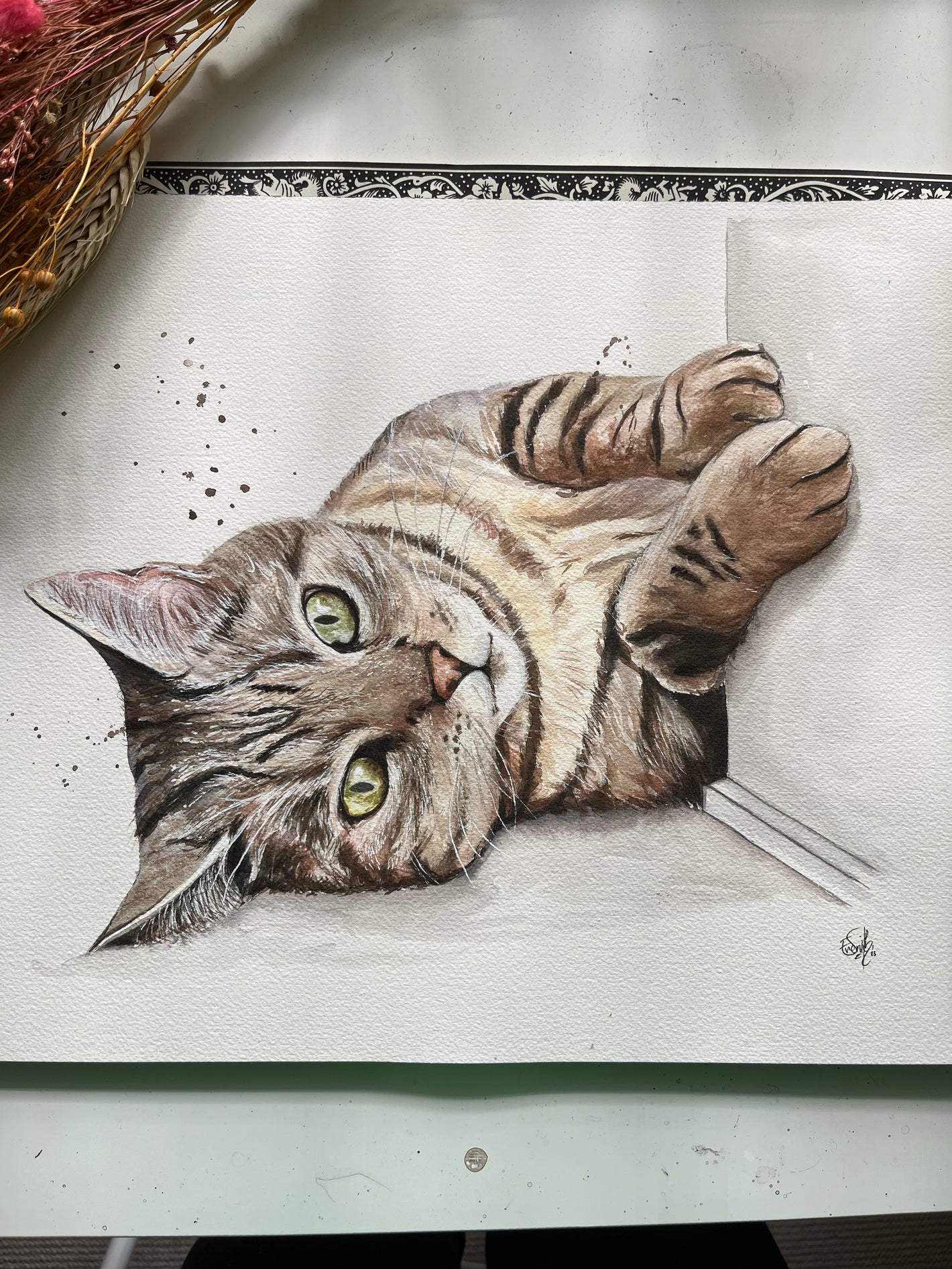 A realistic watercolour portrait of a striped cat laying playfully against a wall. Painted by Grimsby artist, Eve Leoni Smith.
