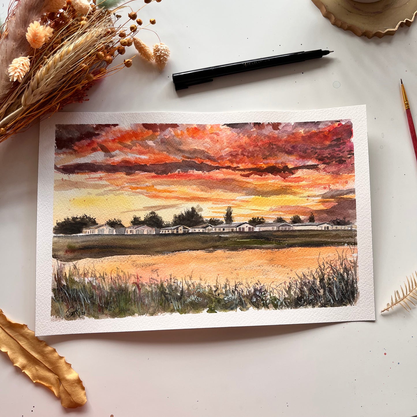 An original watercolour painting by Grimsby artist, Eve Leoni Smith, featuring the caravans at Thorpe Park at Humberston Fitties under a bright orange sunset.