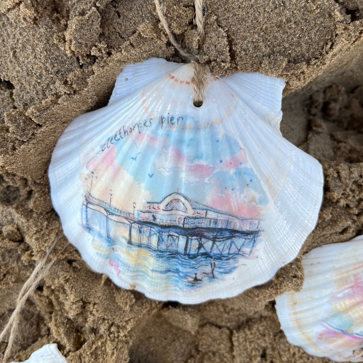 A decorative shell on Cleethorpes beach featuring a watercolour illustration of the Cleethorpes Pier by Eve Leoni Art.