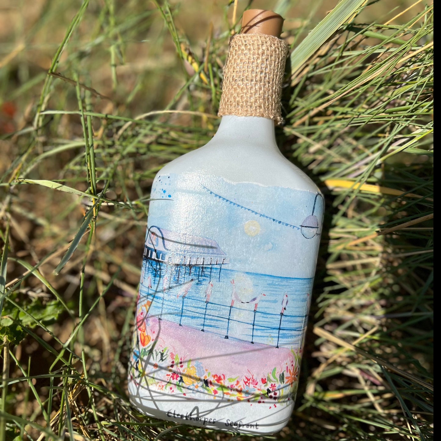 A decoupaged bottle featuring a watercolour illustration of the Cleethorpes Seafront by local artists Eve Leoni Art and Jollypotz.