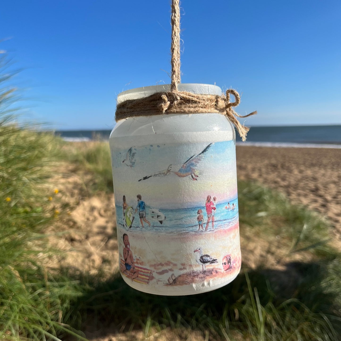 A decoupaged firefly jar featuring watercolour artwork by local artist, Eve Leoni Smith. Cleethorpes beach is in the background.
