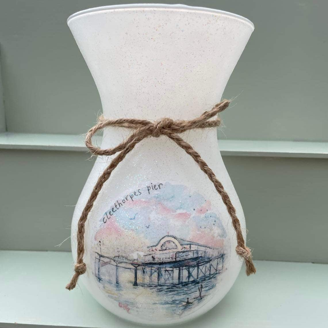 A white vase featuring an illustration of the Cleethorpes Pier by local Grimsby artist, Eve Leoni Smith. Decoupaged by Jollypotz.