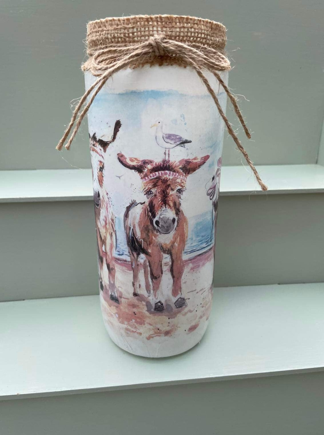 A decoupaged jar on Cleethorpes beach, featuring watercolour artwork of the popular painting 'Donkey Party' by Eve Leoni Smith and Jollypotz.