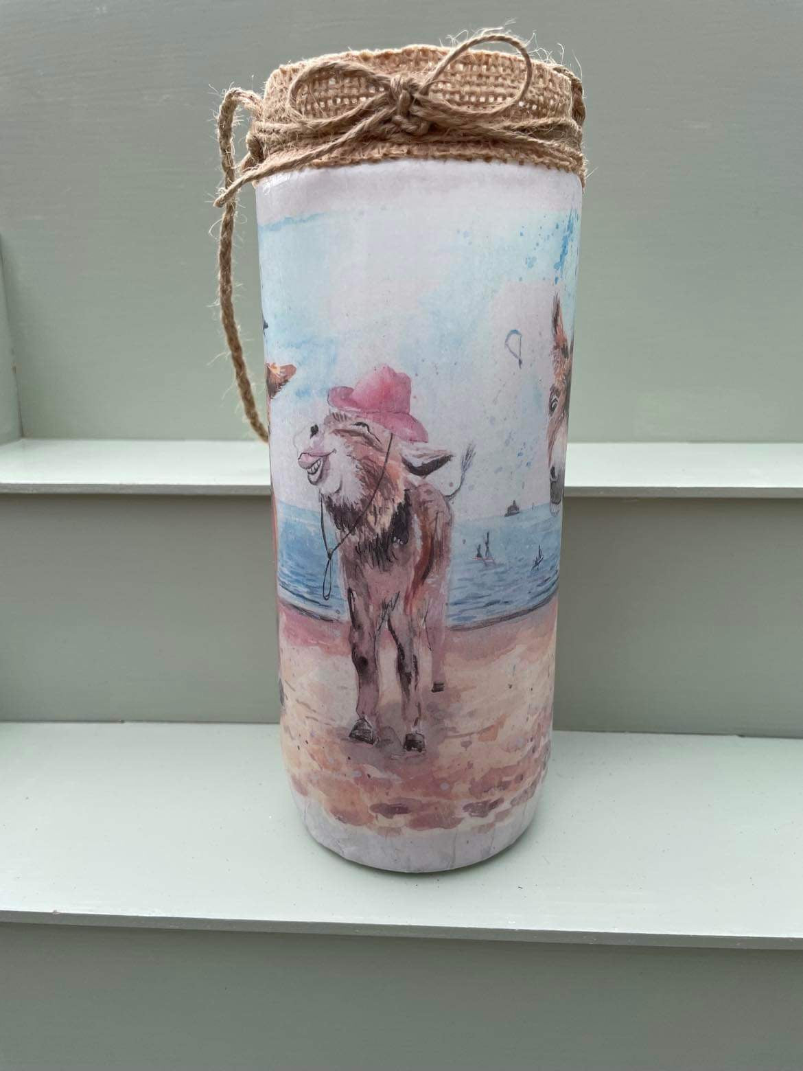 A decoupaged jar on Cleethorpes beach, featuring watercolour artwork of the popular painting 'Donkey Party' by Eve Leoni Smith and Jollypotz.