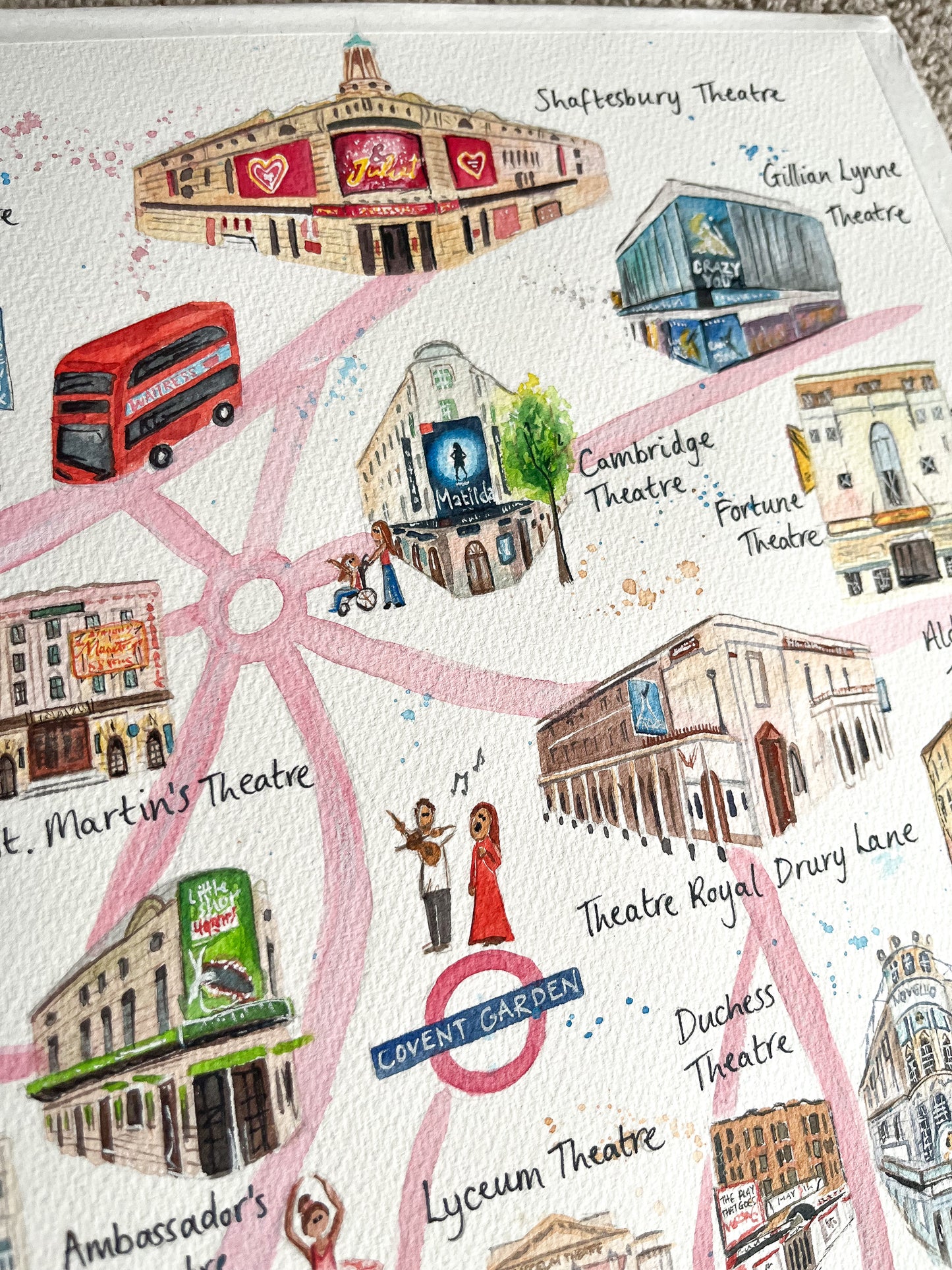 A close up photo of a watercolour map of the West End by artist, Eve Leoni Smith. It includes theatre illustrations of the Shaftesbury Theatre, Theatre Royal Drury Lane and Cambridge Theatre.