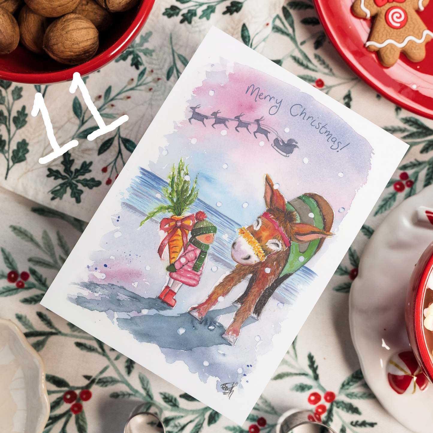 A christmas card featuring a girl on Cleethorpes beach as she surprises Dudley the Donkey with a large carrot for Christmas. Painted by Eve Leoni Smith.