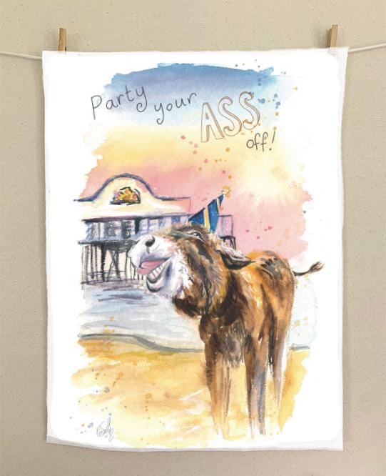 An organic tea towel featuring a watercolour illustration of a donkey showing a happy expression in front of Cleethorpes Pier. He is wearing a blue and yellow party hat, and above reads 'Party your Ass off'. Painted by local Grimsby artist, Eve Leoni Smith.