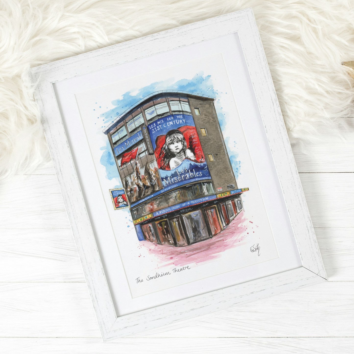 A watercolour illustration of the Sondheim Theatre in London's West End, painted by artist and performer, Eve Leoni Smith. The theatre painting is in a white wooden frame and features the famous musical, Les Miserables.