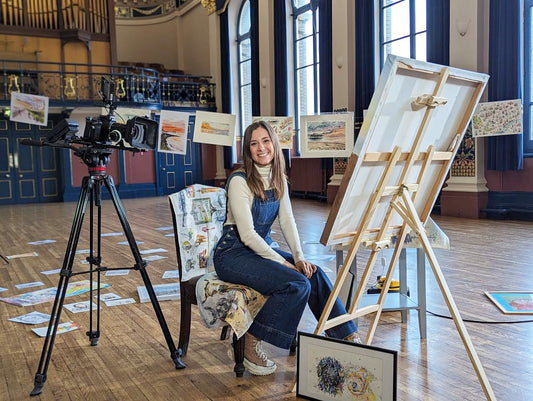 Grimsby artist, Eve Leoni Smith is sat in front of a large canvas surrounded by a gallery of her original watercolour paintings in Grimsby Town Hall. Photo taken by Alex Thompson.