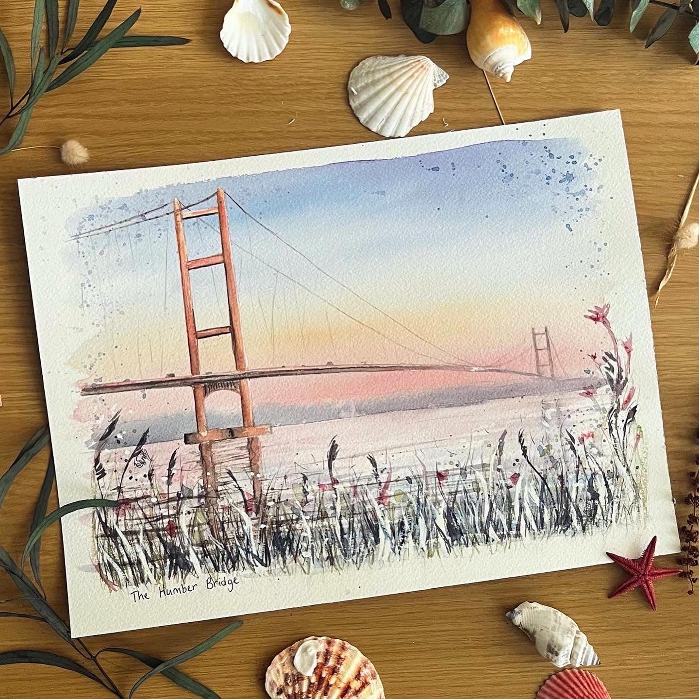 An original watercolour painting by Eve Leoni Smith, featuring the Humber Bridge at sunset with some wildflowers growing in the foreground.