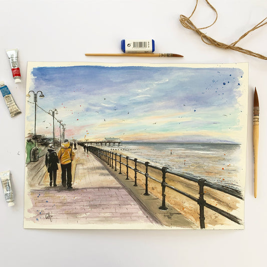 An original watercolour painting of a couple walking along Cleethorpes promenade towards the Cleethorpes Pier on an early winter's evening. Painted by local Grimsby artist, Eve Leoni Smith.