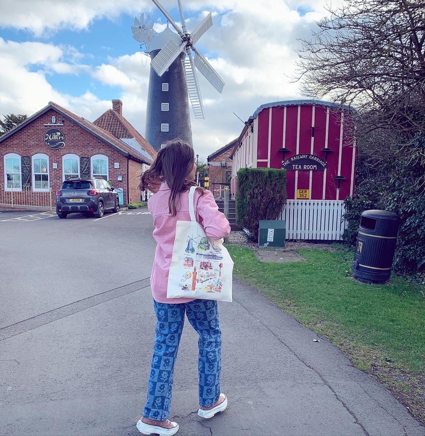 Model holding an Organic tote bag in front of the Waltham Windmill, featuring watercolour illustrations of landmarks in Grimsby and Cleethorpes, designed by local artist, Eve Leoni Smith.