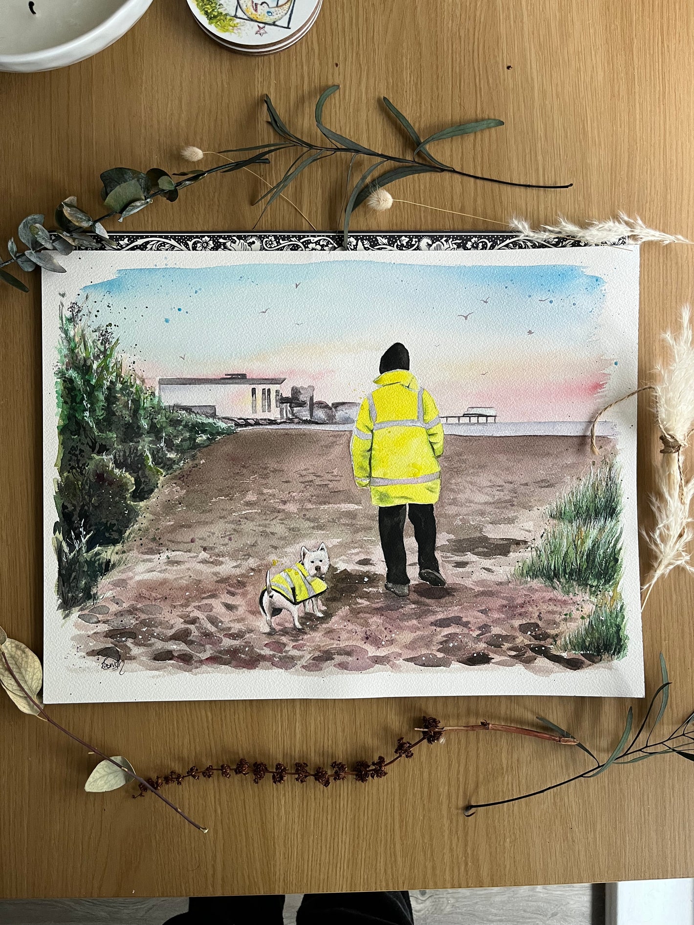 An original watercolour painting of a man and his dog in matching jackets, walking along Cleethorpes beach towards the leisure centre. Painted by Cleethorpes artist, Eve Leoni Smith.