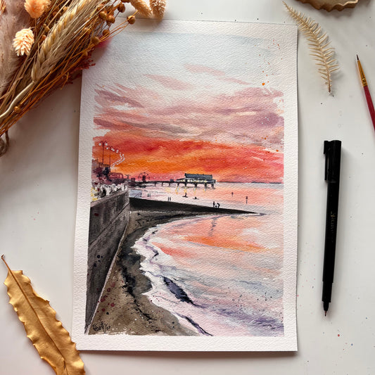 An original watercolour painting by Cleethorpes artist, Eve Leoni, of Cleethorpes beach at sunset. The pier, promenade and some paddleboarders can be seen in the distance. 