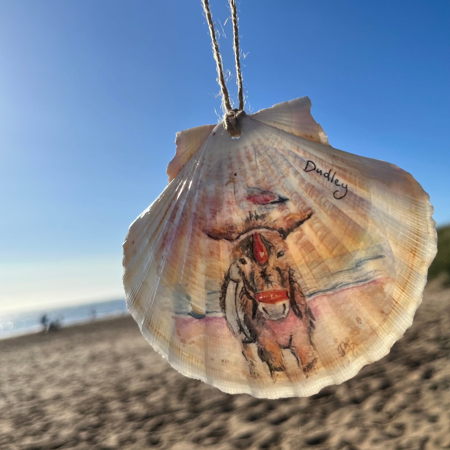 A decoupaged shell featuring a watercolour illustration of Dudley the Donkey on Cleethorpes beach, by local artist Eve Leoni Art and Jollpotz.