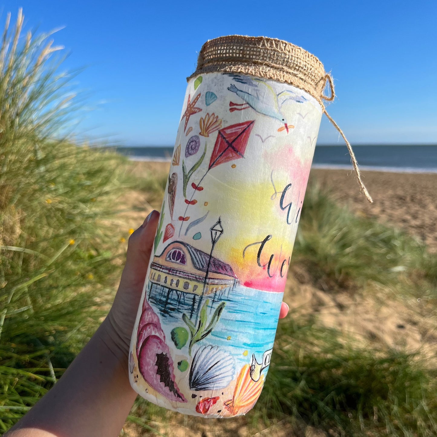 A decoupaged jar on Cleethorpes beach featuring watercolour artwork by local artist, Eve Leoni Smith. 