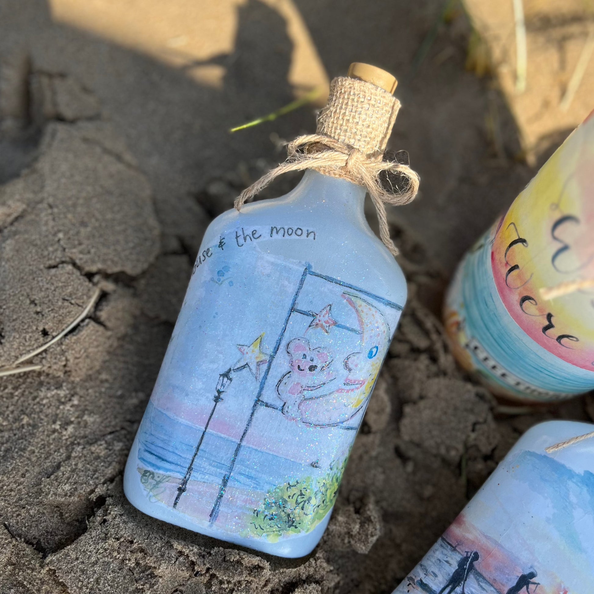 A decoupaged jar on Cleethorpes beach, featuring watercolour artwork of the Mouse and the Moon by Eve Leoni Smith and Jollypotz.