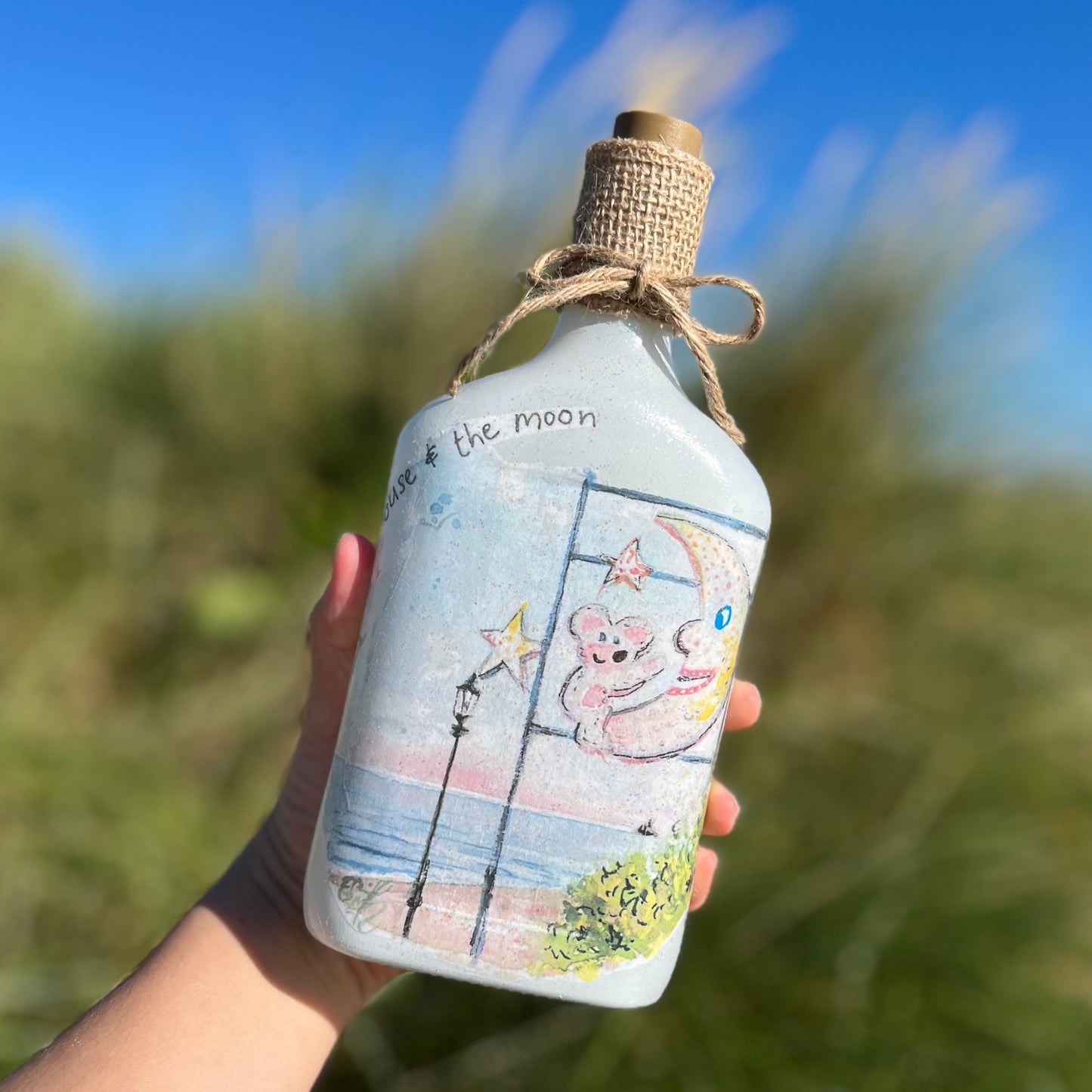 A decoupaged jar on Cleethorpes beach, featuring watercolour artwork of the Mouse and the Moon by Eve Leoni Smith and Jollypotz.