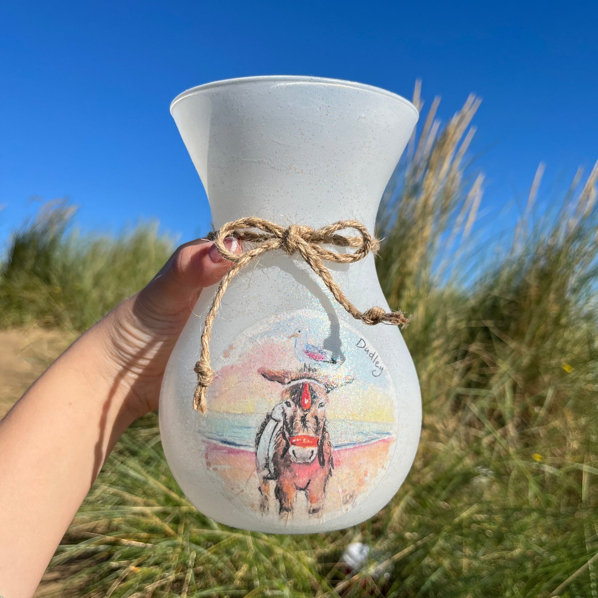 A decoupaged vase on Cleethorpes beach, featuring watercolour artwork of Dudley the Donkey by Eve Leoni Smith and Jollypotz.