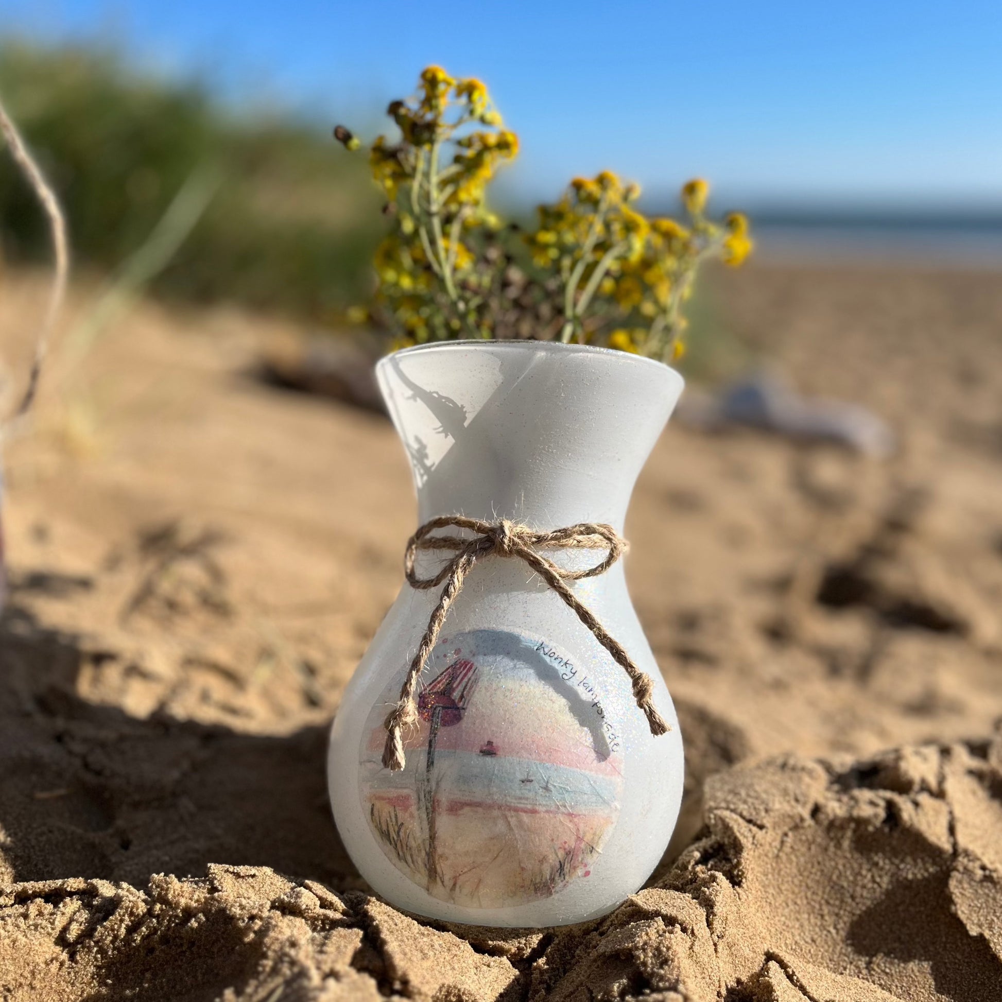 A decoupaged vase on Cleethorpes beach, featuring watercolour artwork of Humberston Fitties Beach by Eve Leoni Smith and Jollypotz.