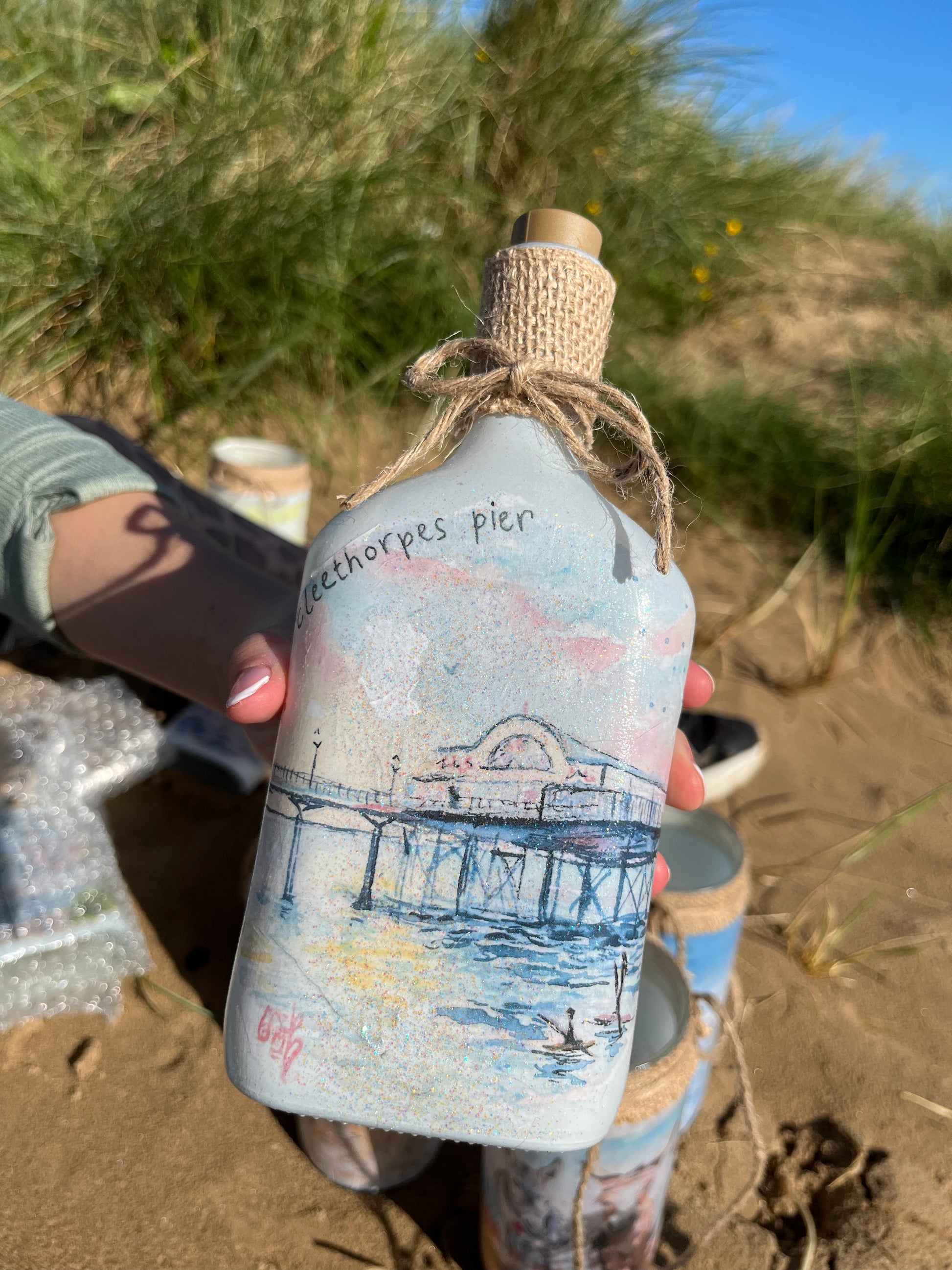 A decoupaged bottle as featuring watercolour artwork of the Cleethorpes pier by Eve Leoni Smith and Jollypotz.
