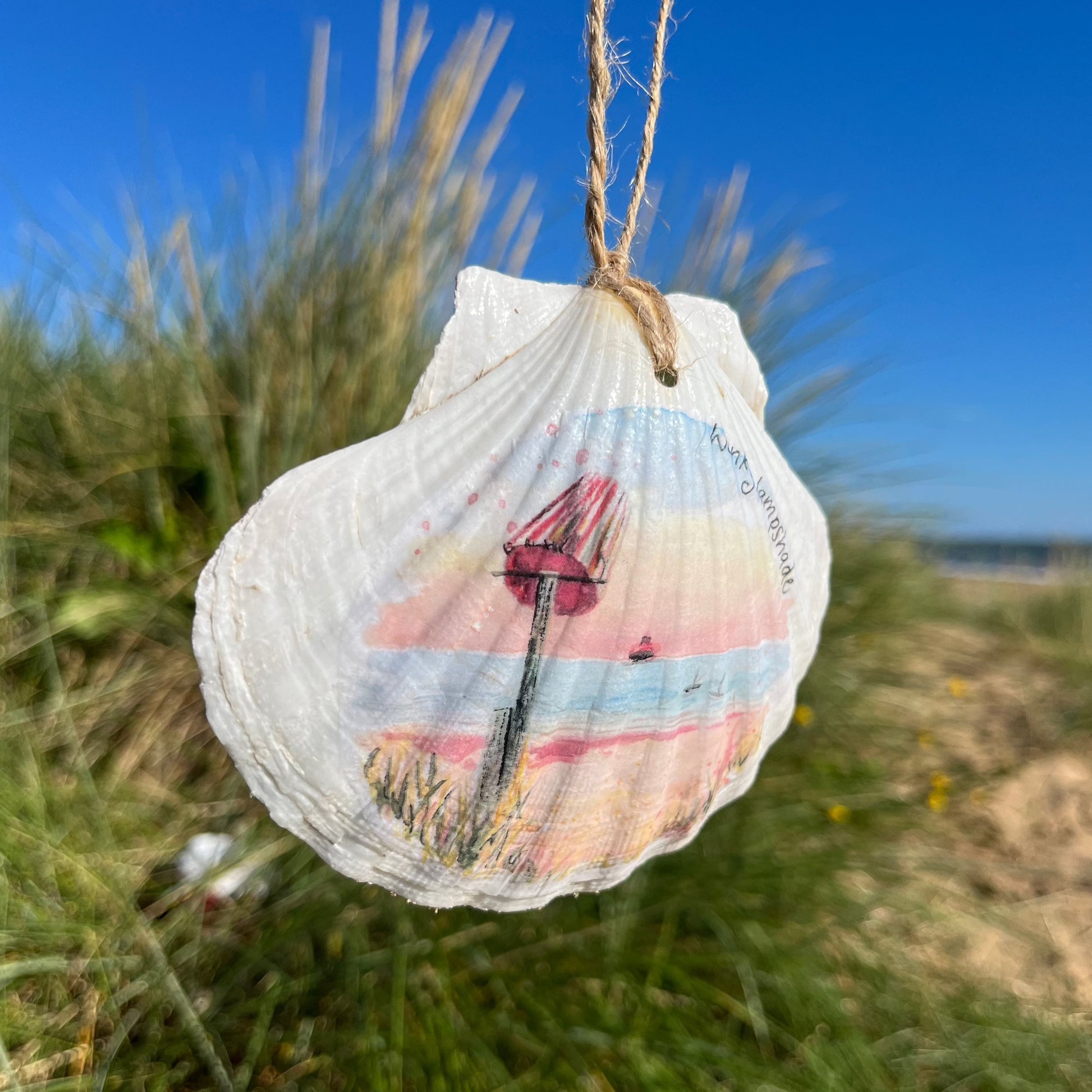 A decoupaged shell on Cleethorpes beach, featuring watercolour artwork of Humberston Fitties Beach by Eve Leoni Smith and Jollypotz.