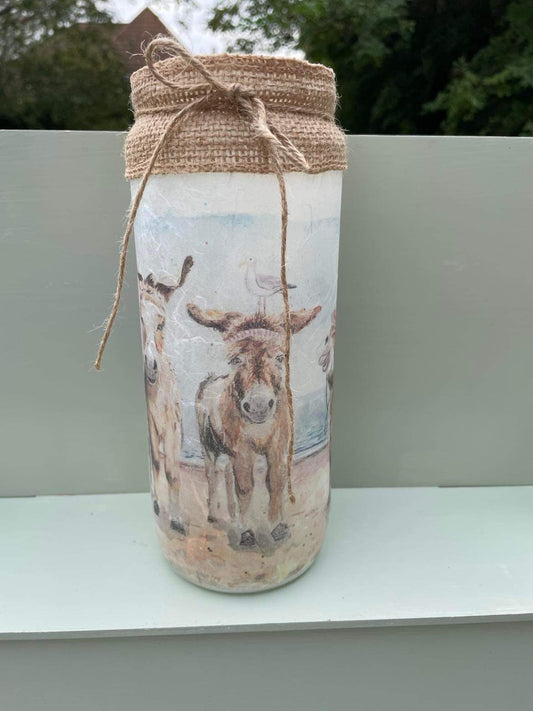 A decoupaged jar on Cleethorpes beach, featuring watercolour artwork of the popular painting 'Donkey Party' by Eve Leoni Smith and Jollypotz.