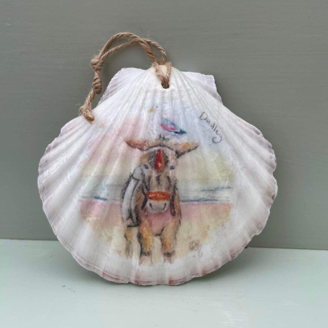 A decoupaged shell featuring a watercolour illustration of Dudley the Donkey on Cleethorpes beach, by local artist Eve Leoni Art and Jollpotz.