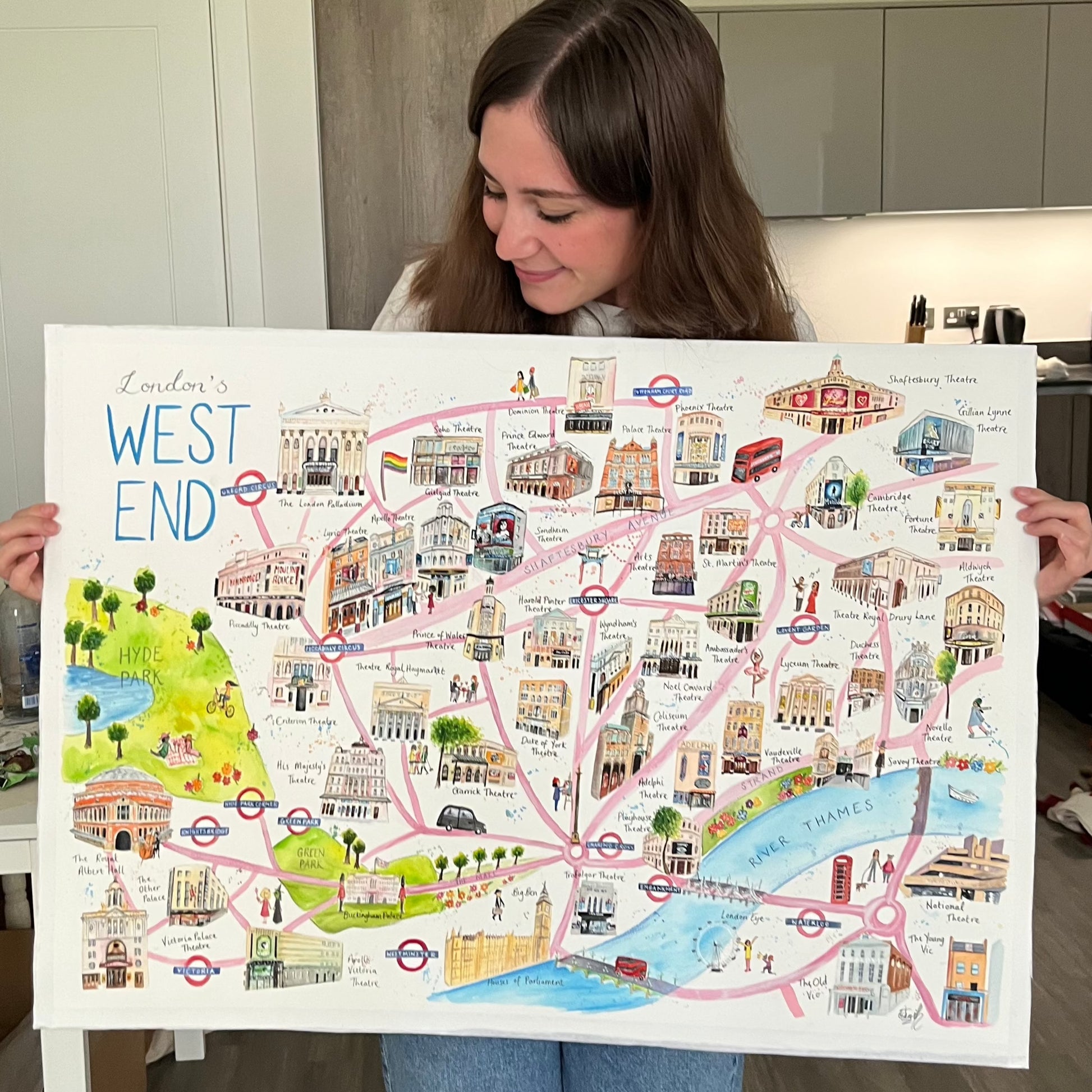 Artist and performer, Eve Leoni Smith, holding a watercolour map of the West End featuring all the West End theatres in London.