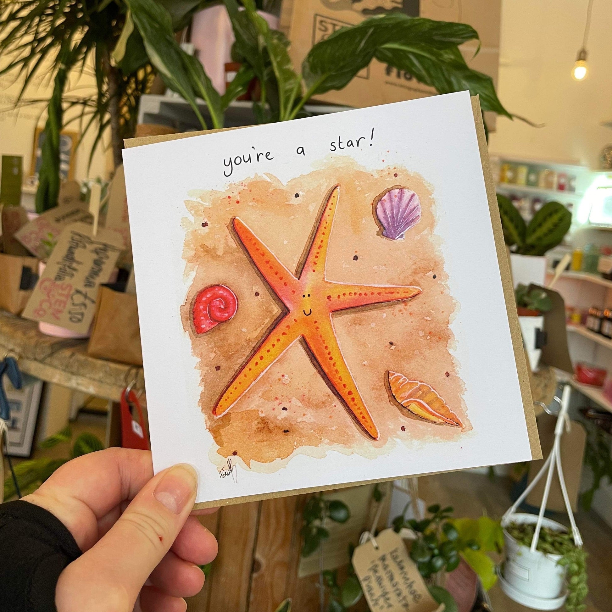 A cheerful greetings card designed by Eve Leoni Smith, featuring a starfish illustration and the quote, 'You're a star!'.