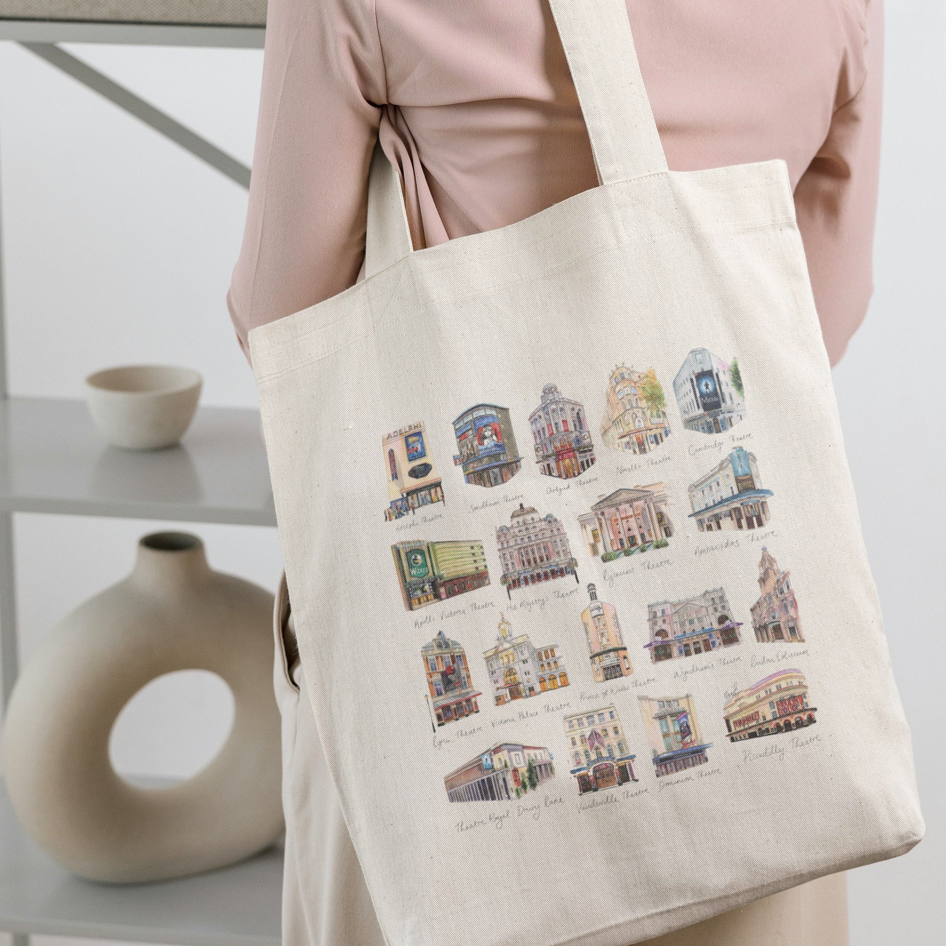 Person holding a tote bag with colorful theatre illustrations in a minimal indoor setting by Eve Leoni Art.