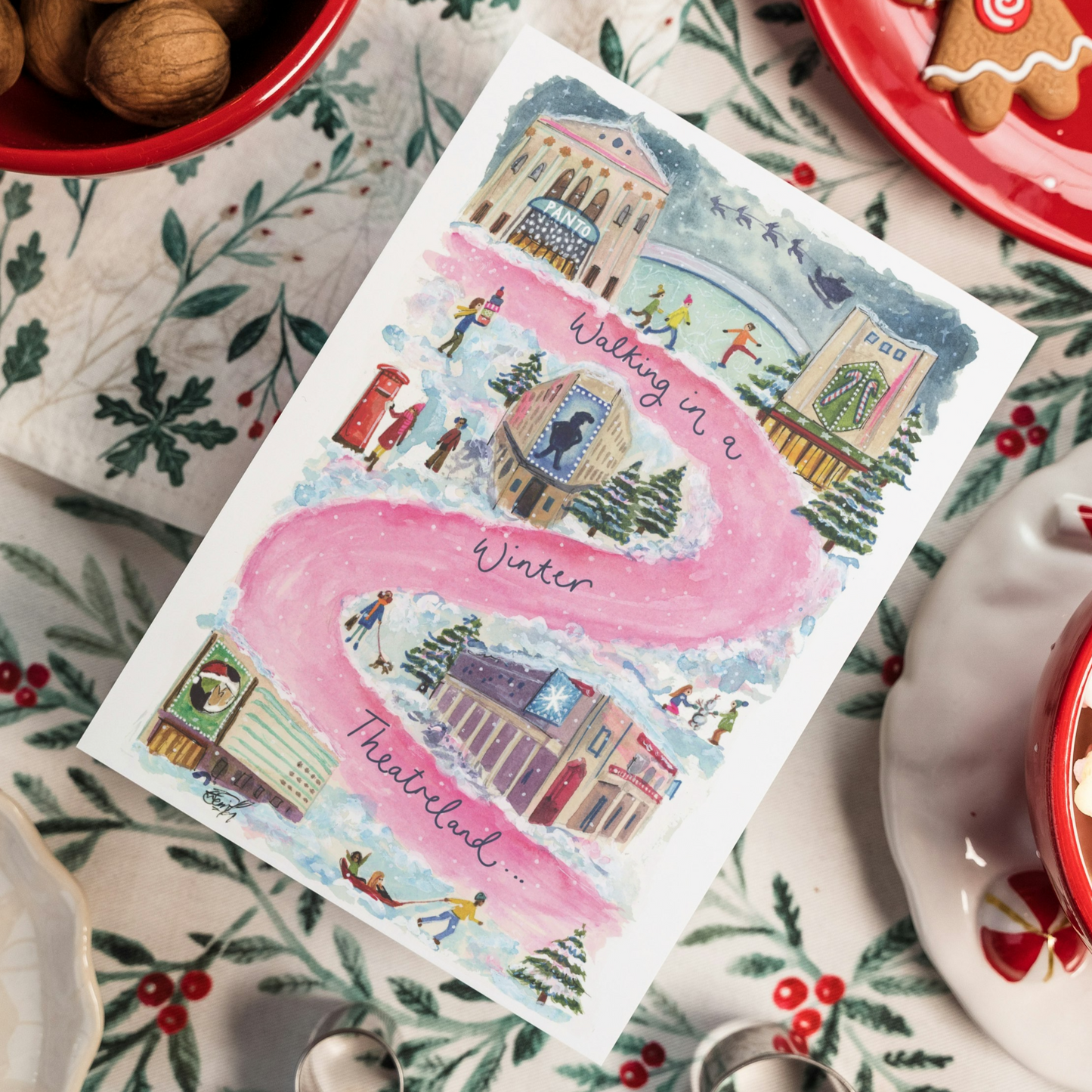 A West End Christmas card featuring watercolour artwork by artist and performer Eve Leoni Art. The painting shows a pink road swirling through West End theatres such as the London Palladium, Cambridge Theatre and Theatre Royal Drury Lane during winter.