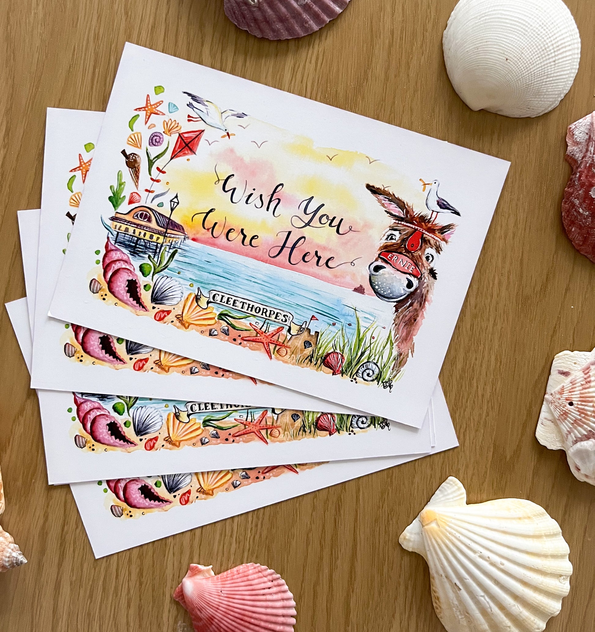 Cleethorpes postcards designed by Eve Leoni Art for local author, Tracy Baines. The design features the Cleethorpes pier and a donkey along with the writing, 'wish you were here'.