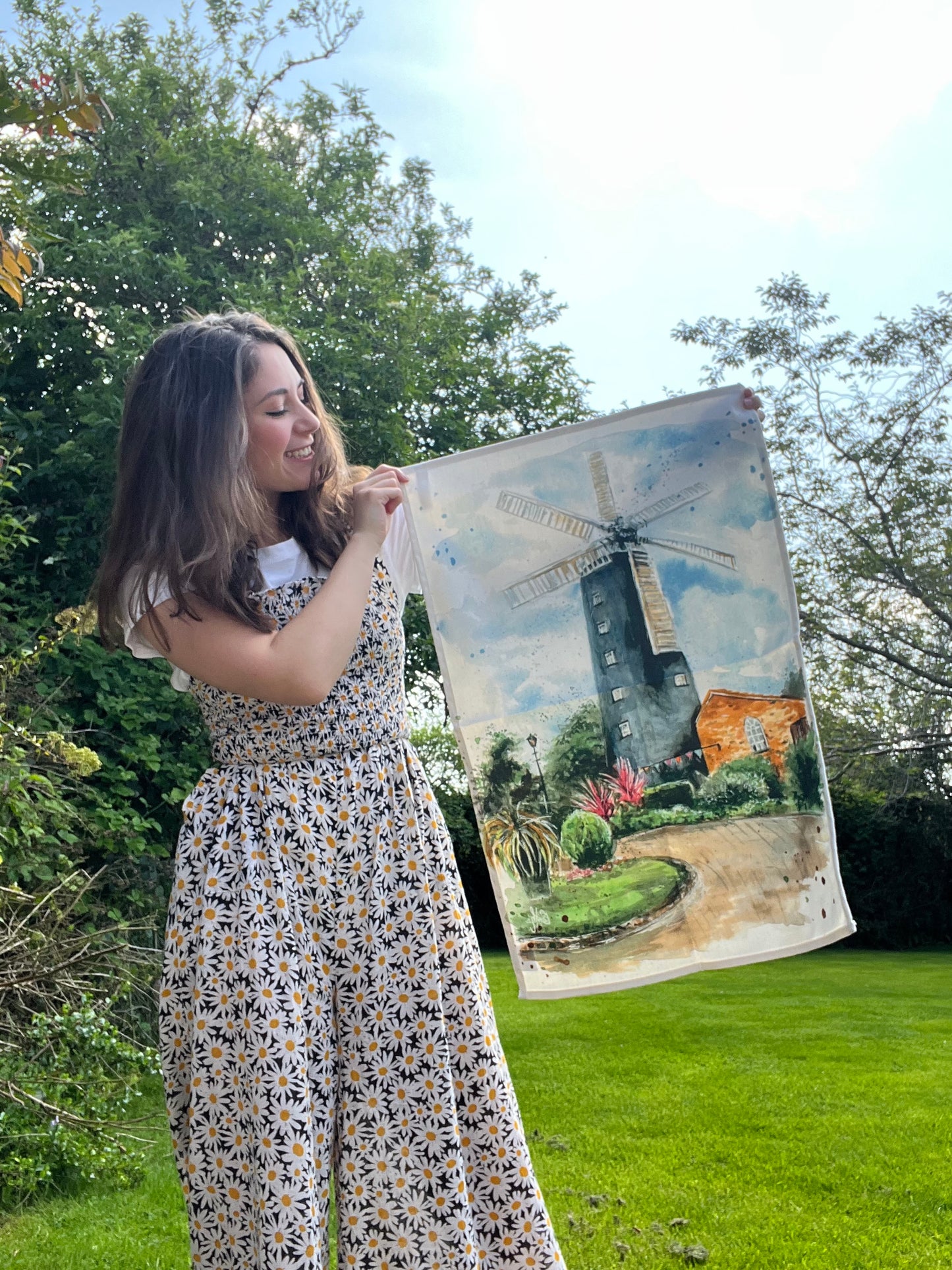 Local Lincolnshire artist, Eve Leoni Smith, holding up an organic tea towel featuring her original watercolour artwork of the Waltham Windmill.