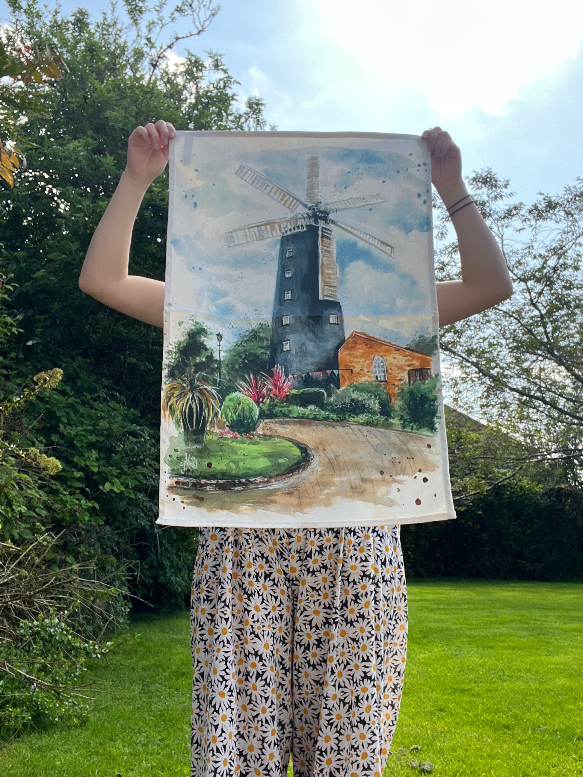Grimsby artist, Eve Leoni, holding up an organic tea towel featuring artwork of the Waltham Windmill.